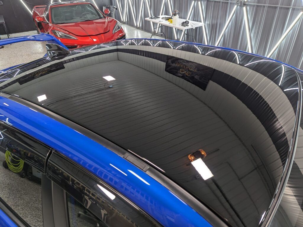 A blue car with a black roof is sitting in a garage next to a red car.