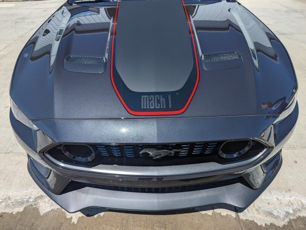 A gray mustang with a red stripe on the hood