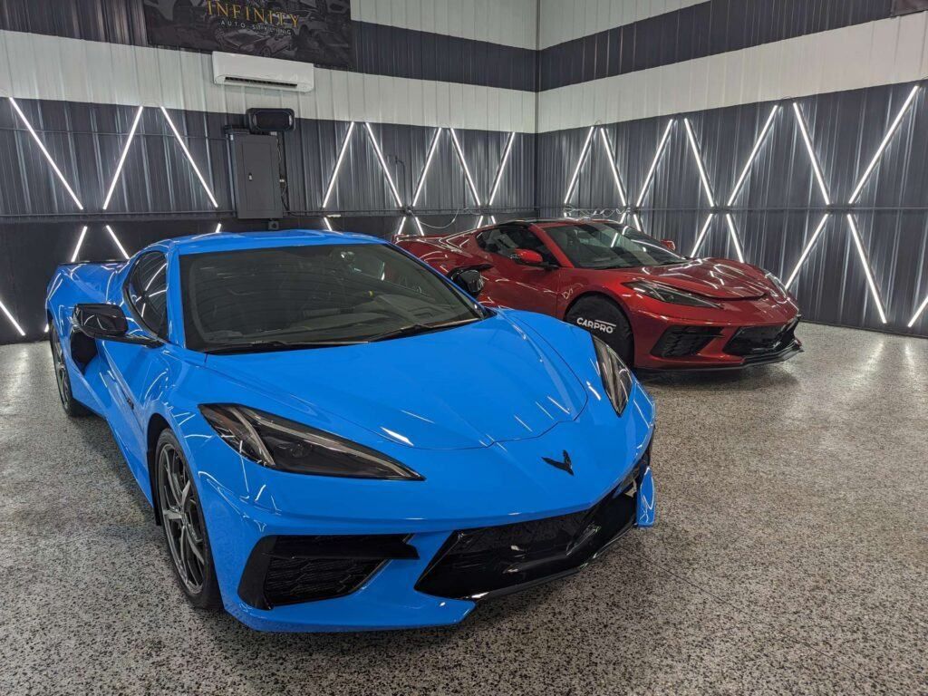 A blue corvette is parked next to a red corvette in a garage.