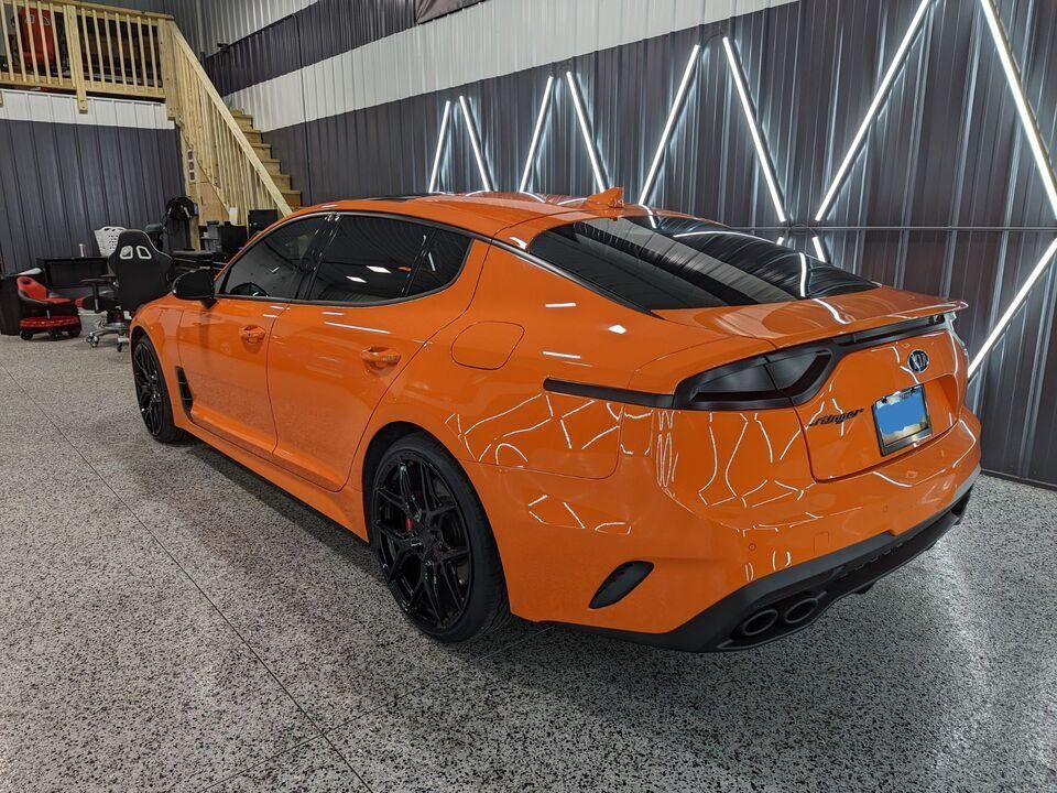 A orange car is parked in a garage next to a staircase.