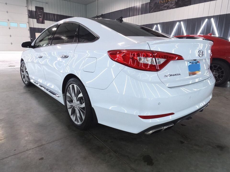 A white car is parked in a garage next to a red car.