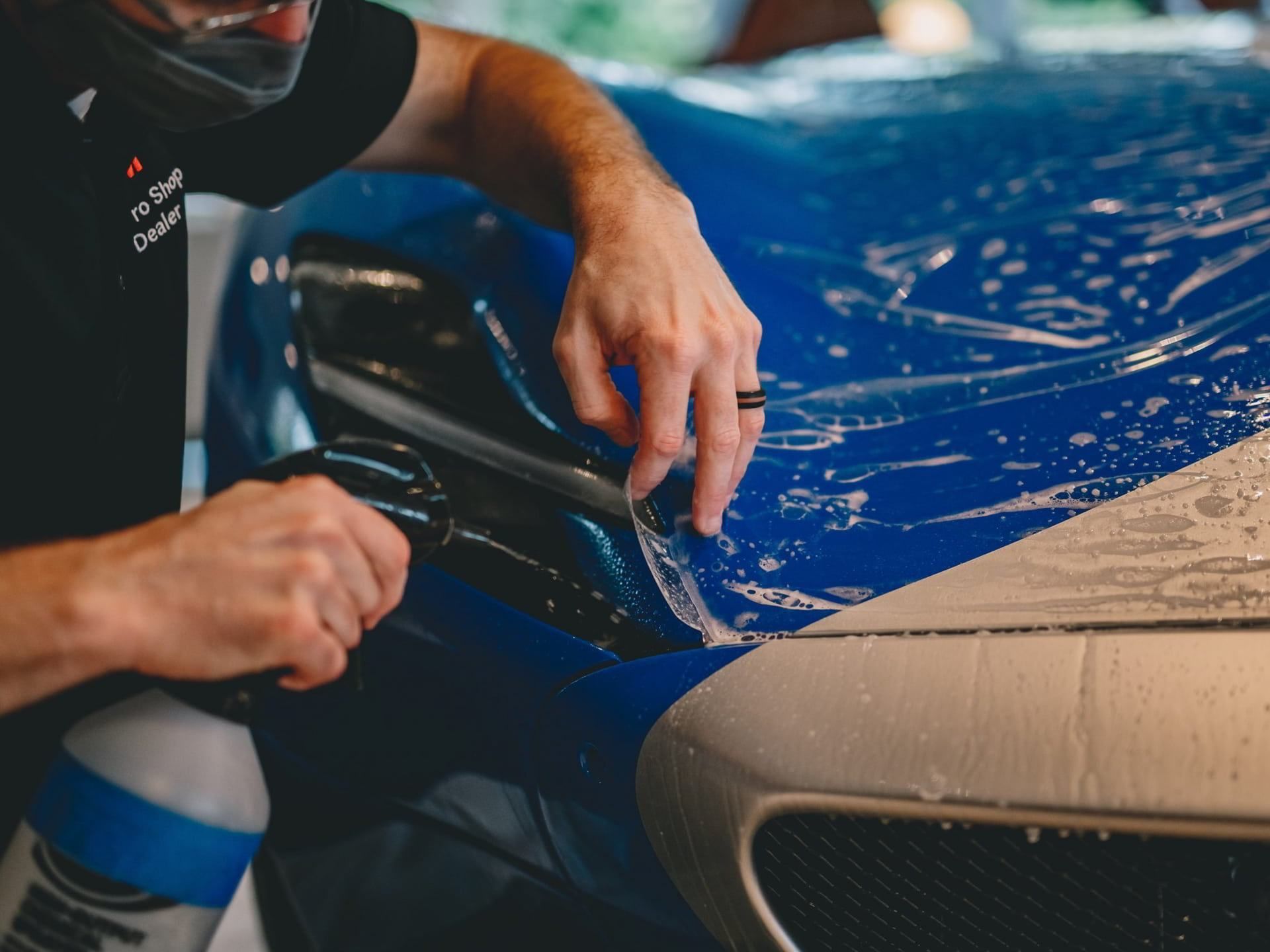 A man is wrapping a blue car with plastic wrap.