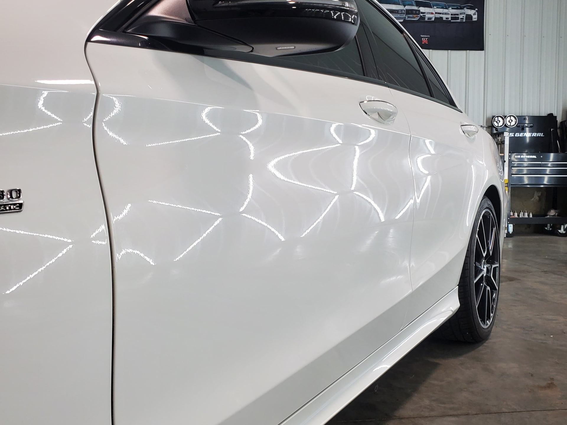 A white car is parked in a garage with a picture on the wall behind it.