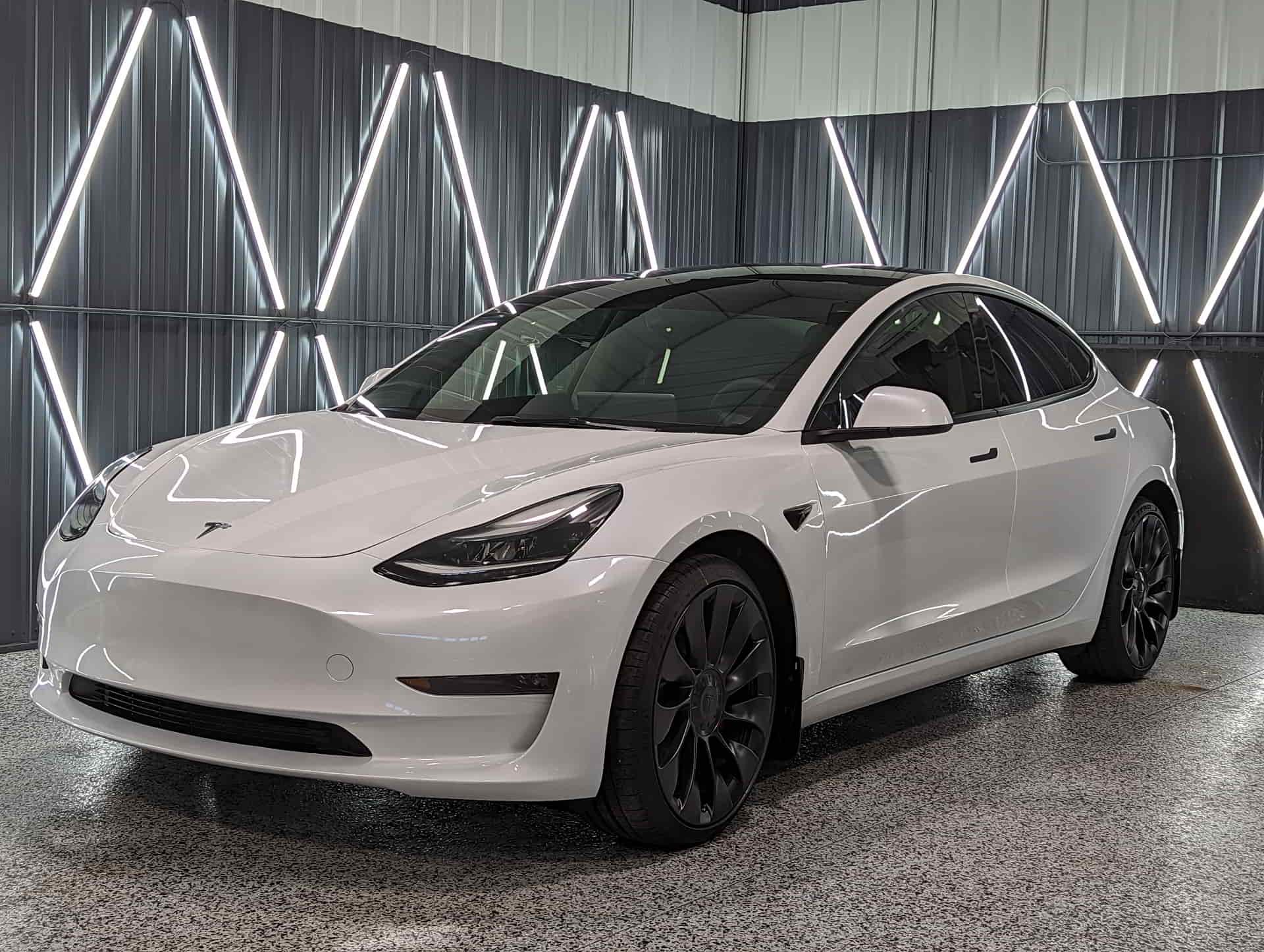 A white tesla model 3 is parked in a garage.