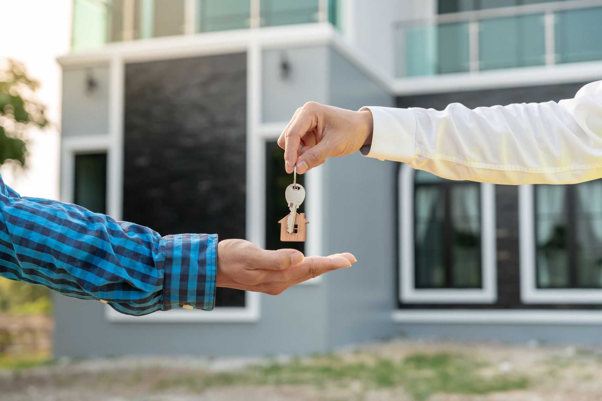A man is handing a key to another man in front of a house.