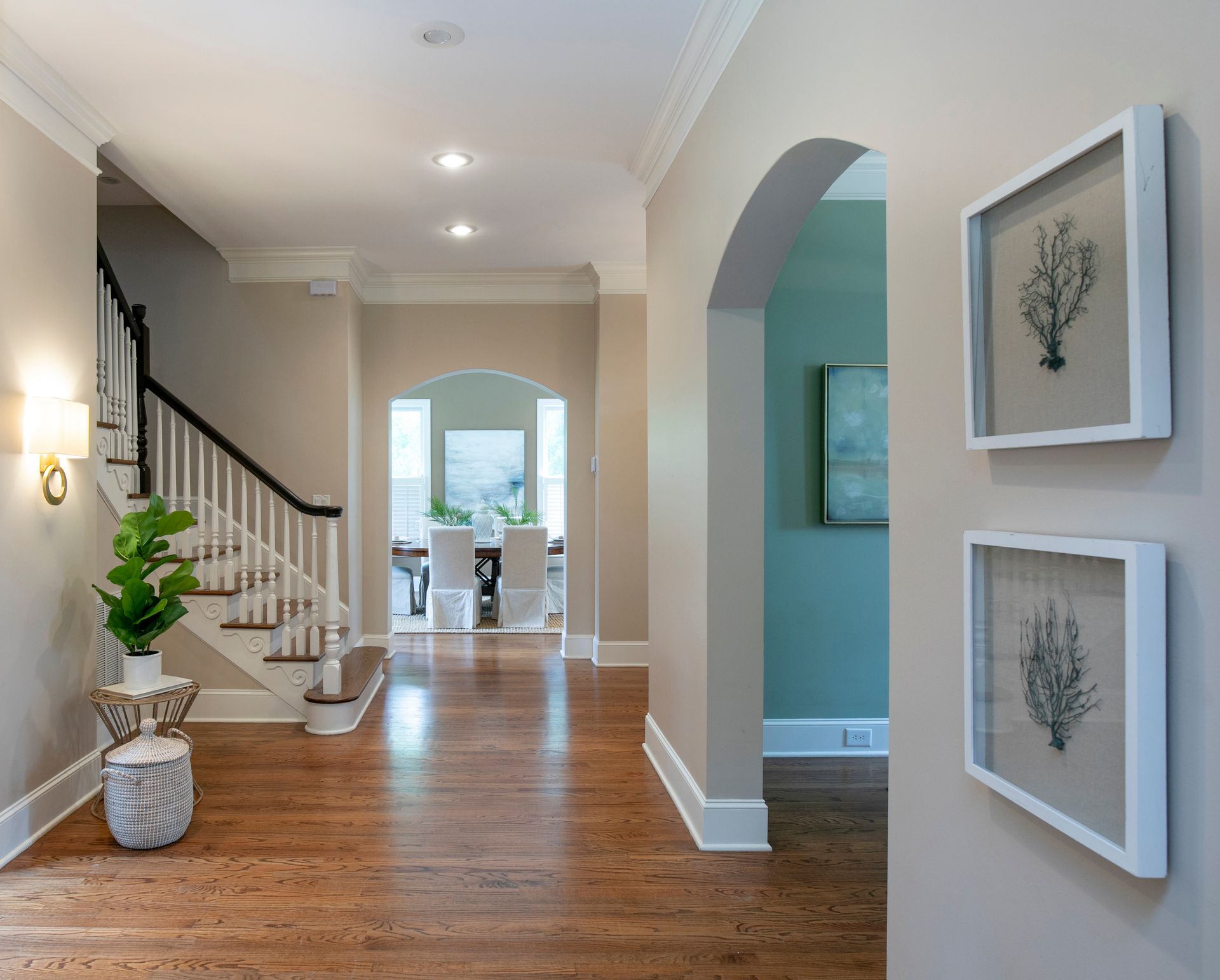 A hallway in a house with a staircase and paintings on the wall.
