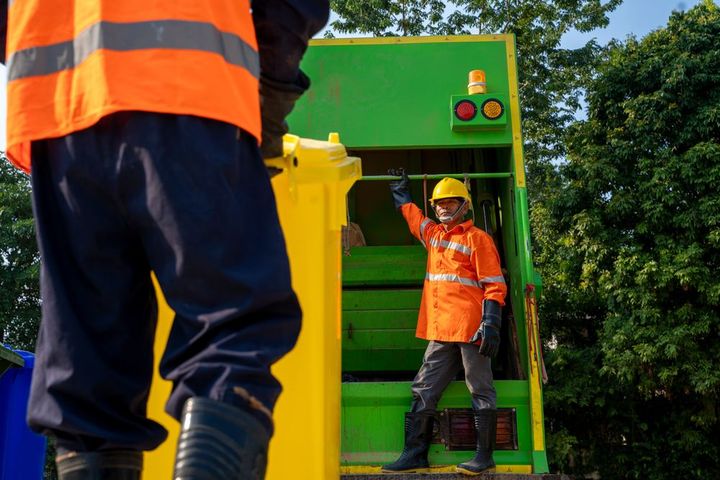 a man in an orange vest is standing next to a garbage truck .