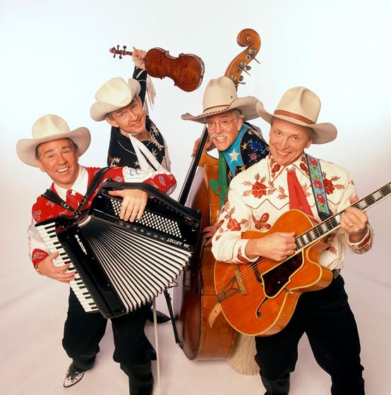 Four gentlemen holding instruments and smiling, all wearing cowboy hats and western apparel. 