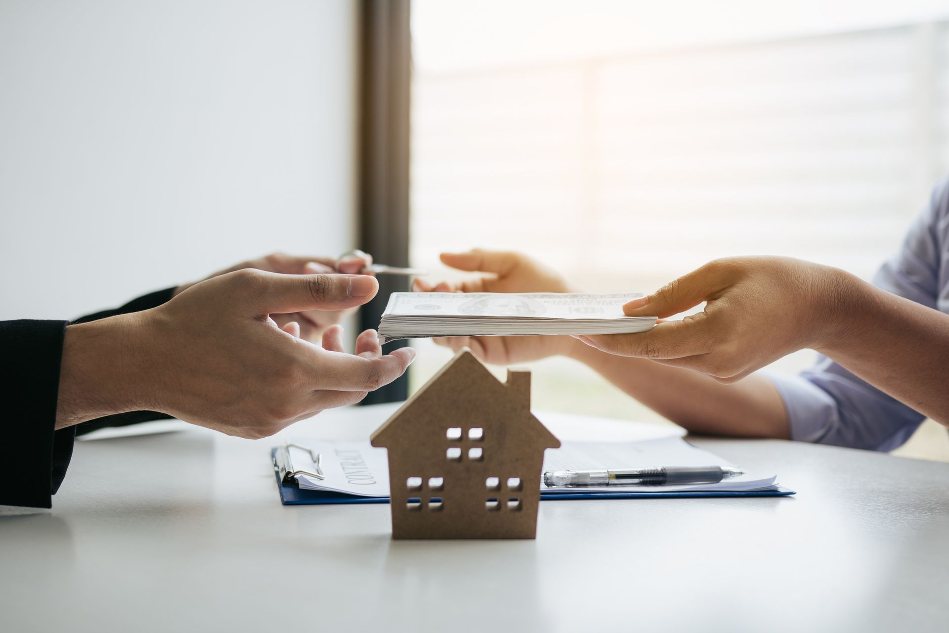 A person is holding a piece of paper in front of a model house.