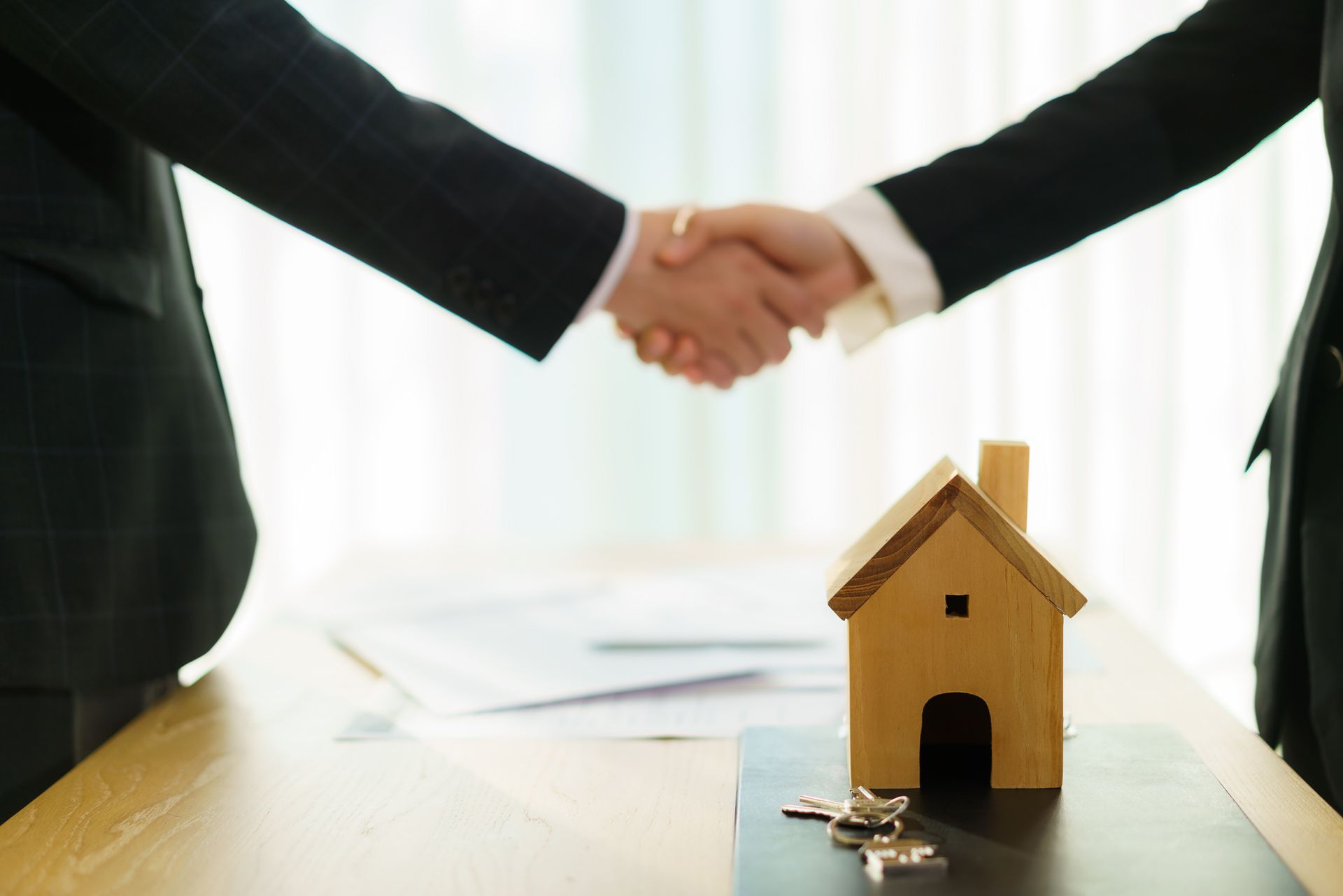 Two people are shaking hands over a table with a model house and keys.