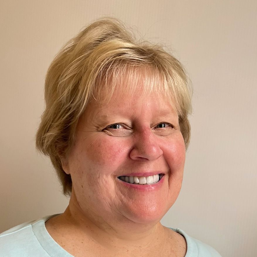 Smiling woman with short blonde hair, wearing a light blue shirt, looking at the camera.
