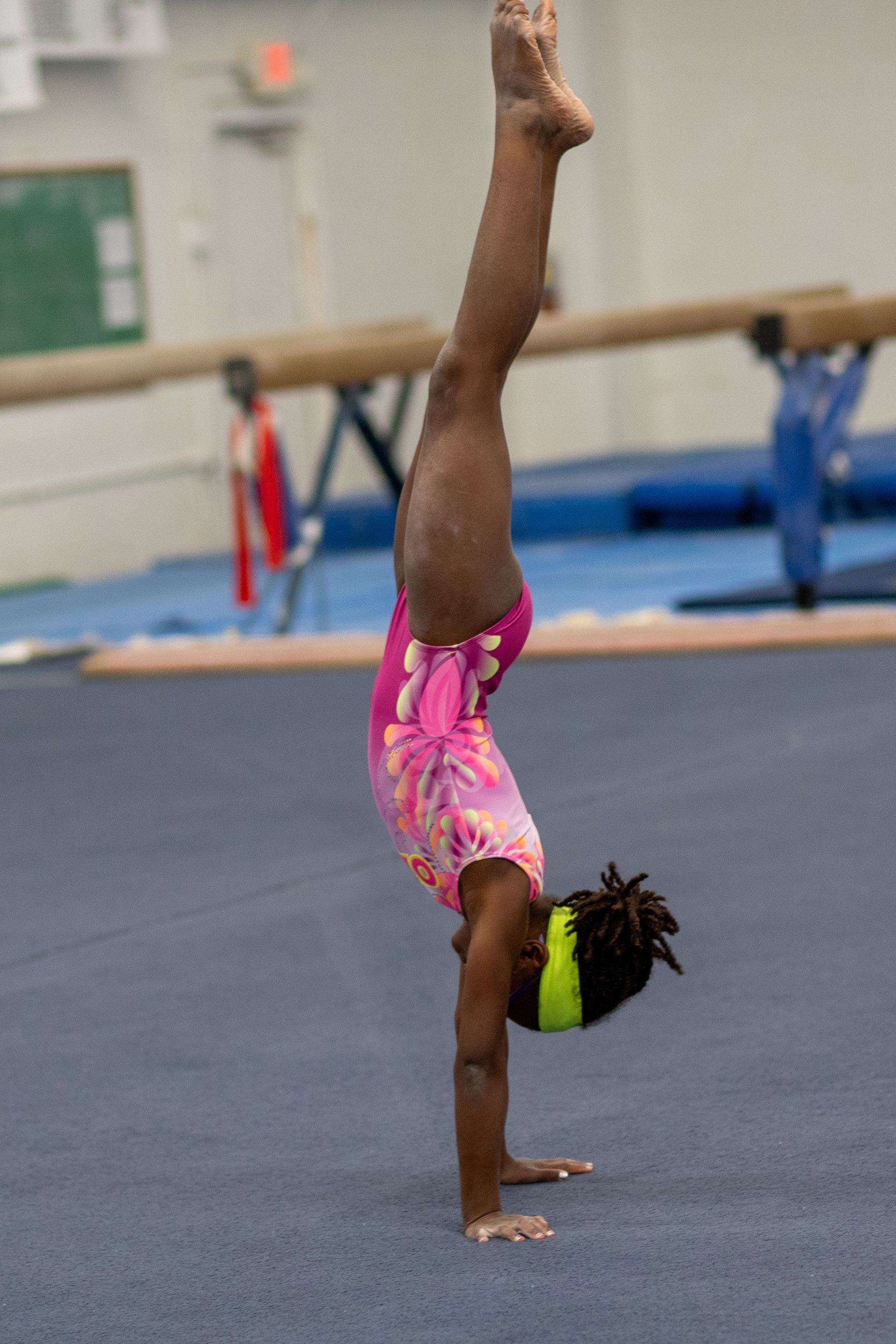 A young girl jumps in the air, high-fiving a taller woman on a red mat in a gymnastics gym.