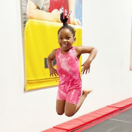 Young girl in pink leotard jumping on trampoline, smiling, in gym.