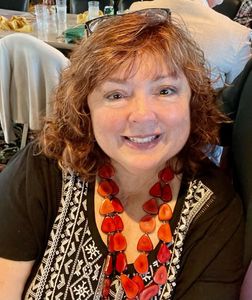 A woman wearing a black shirt and a red necklace is smiling for the camera.