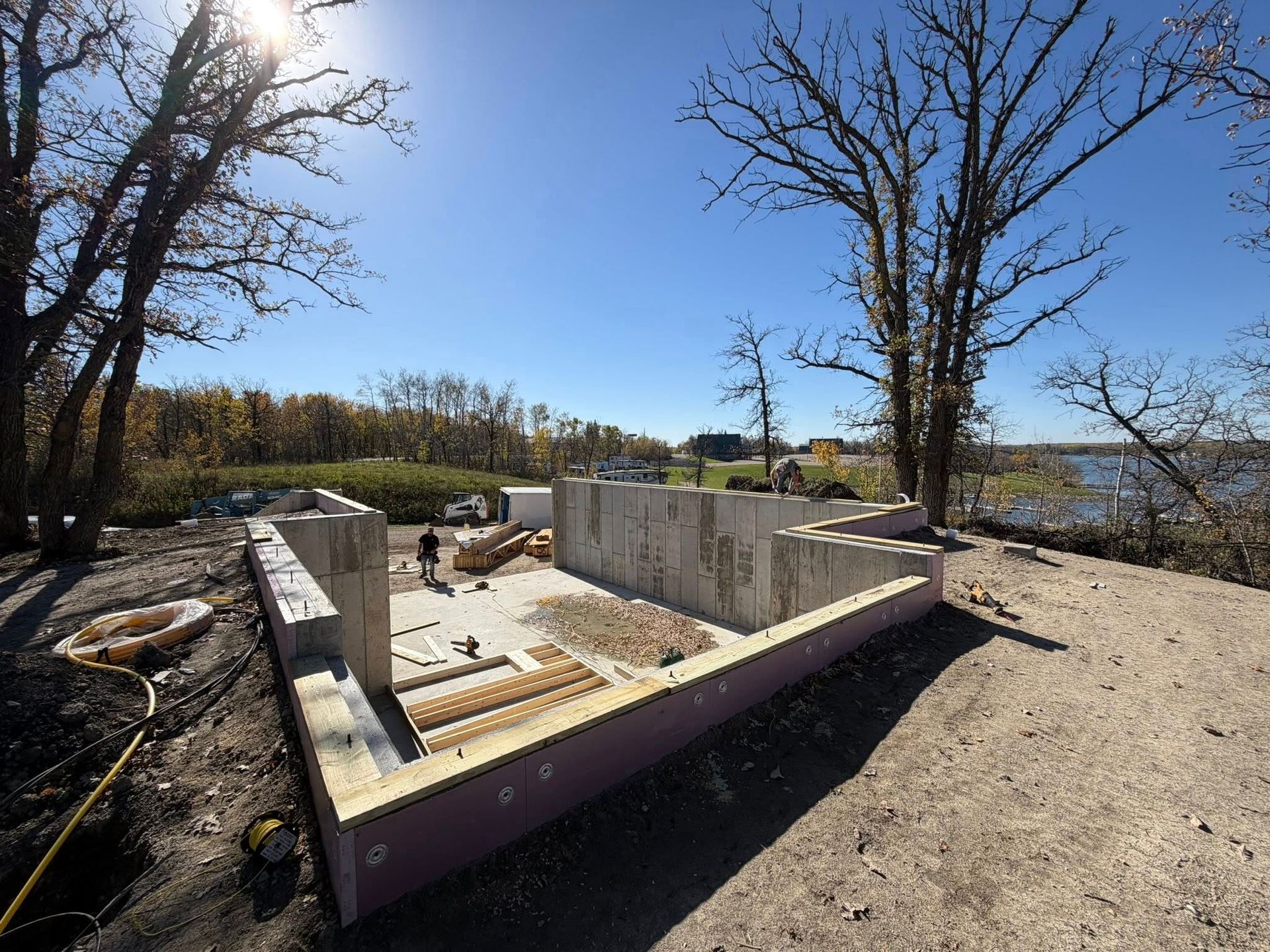 Foundation of a building under construction on a sunny day near trees and water.