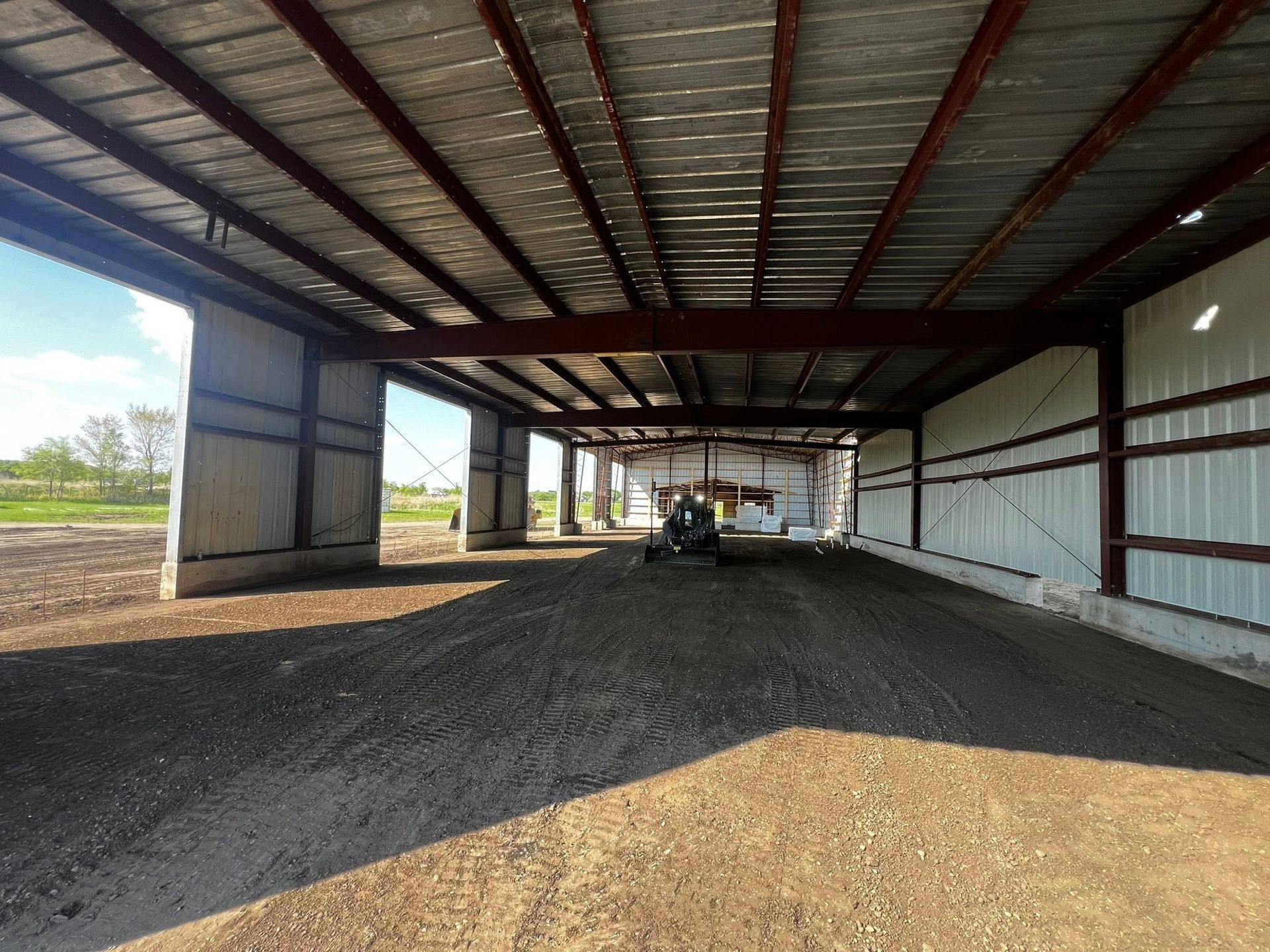 Open-sided metal shed with a dirt floor, open doorway, and a small machine inside.