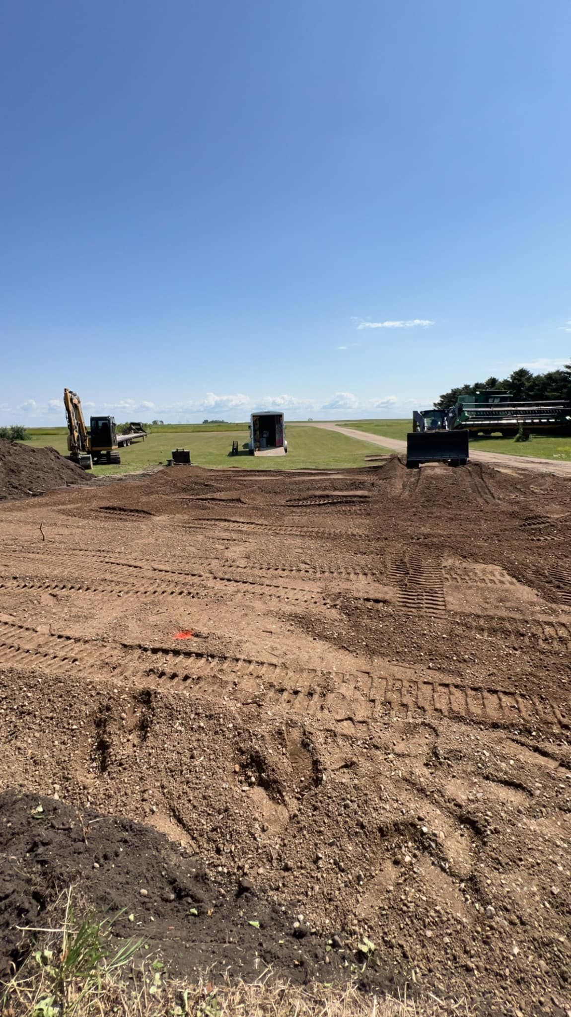 Construction site with dirt piles, excavator, and truck on a bright, sunny day.
