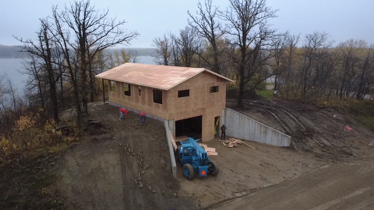 Construction of a building on a hillside; blue tractor, workers, lake in background.