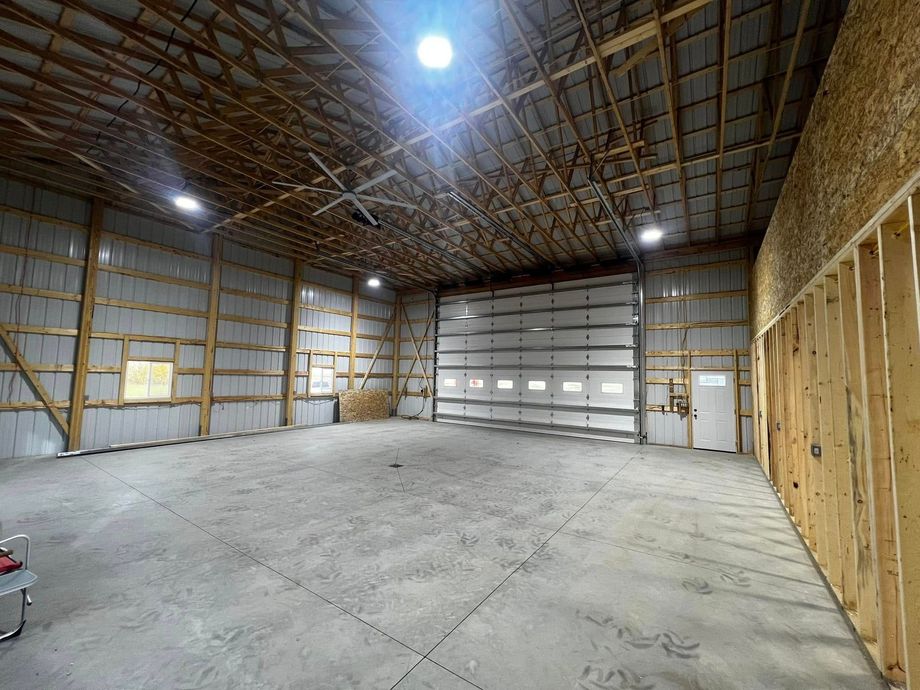 Empty warehouse interior with concrete floor, overhead door, exposed rafters, and framing.