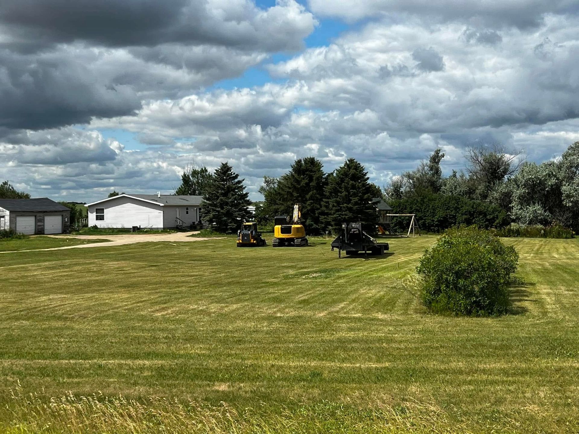 Open field with construction equipment near a white house under a cloudy sky.