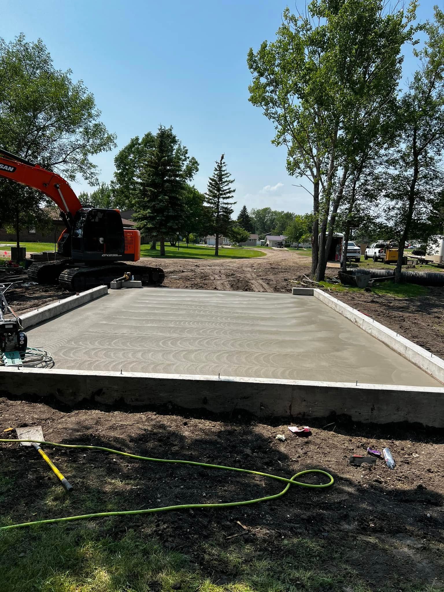 Freshly poured concrete slab bordered by low walls; construction site, trees, clear sky.