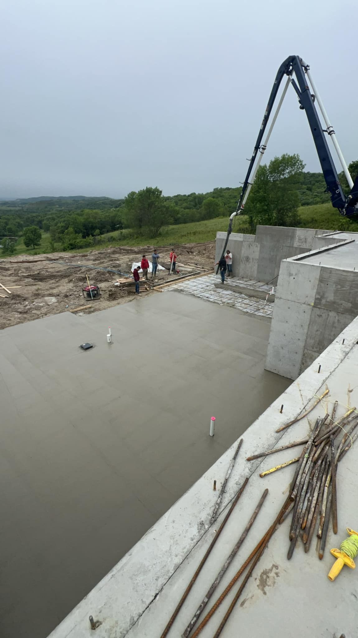 Concrete being poured by a pump truck on a construction site; workers stand by; overcast day.