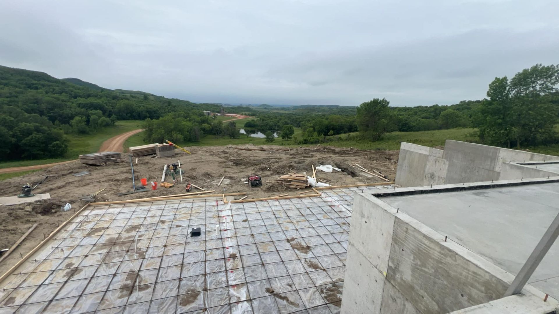 Construction site overlooking a valley, concrete foundations in foreground, cloudy sky.