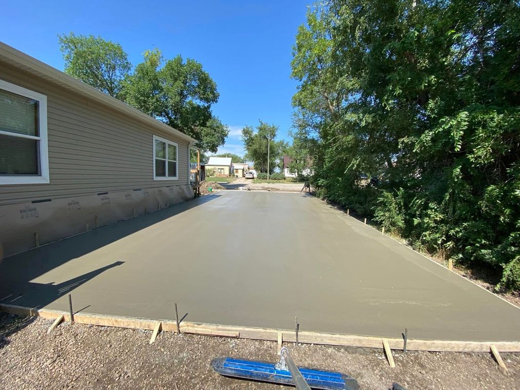 Newly poured concrete driveway next to a beige house, under a clear blue sky.