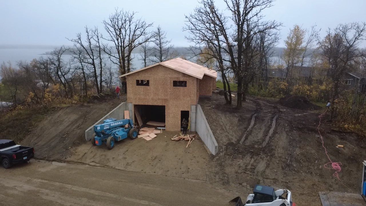 Construction of a two-story building on a hillside. Exterior framing visible. Heavy machinery and muddy ground.