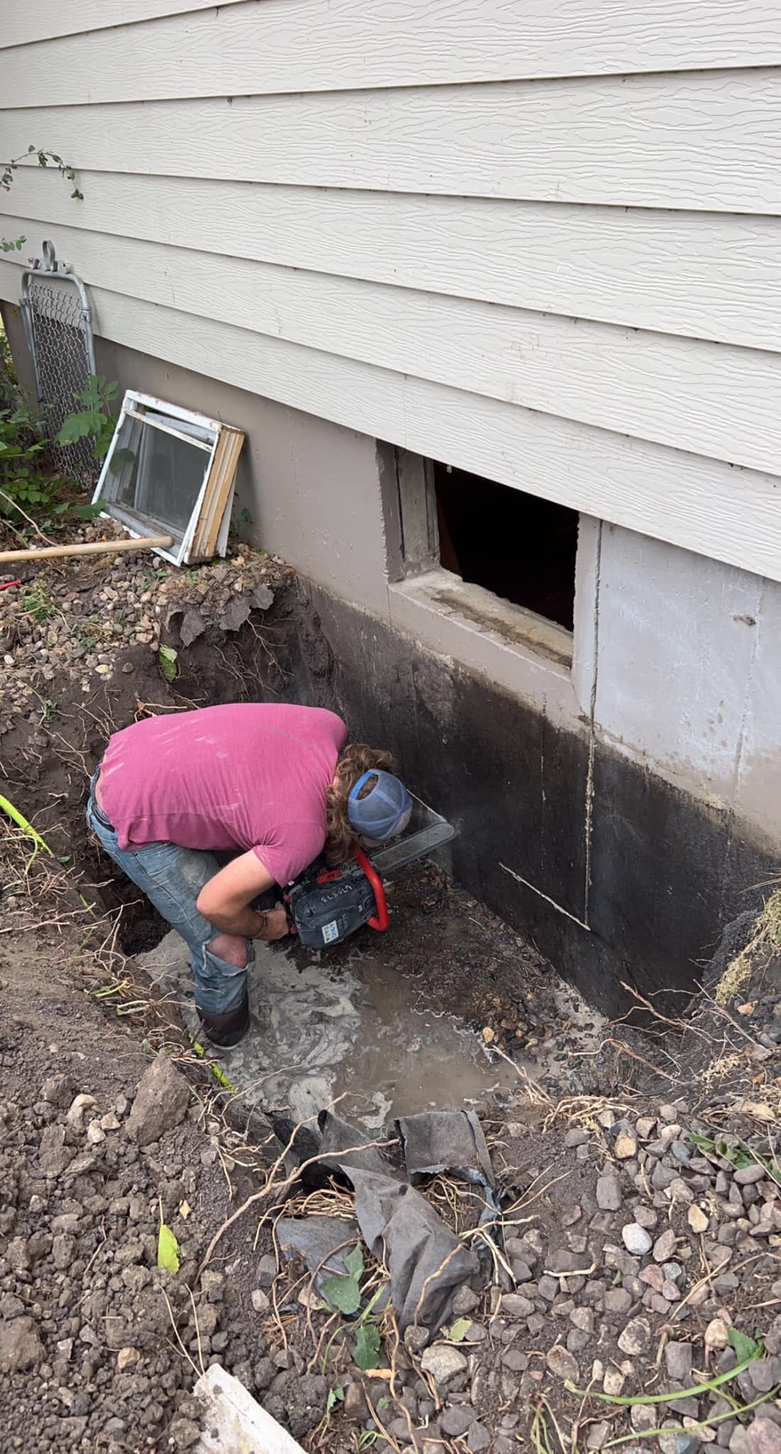 Person using a saw to cut a foundation wall outdoors. Dirt surrounds the foundation.