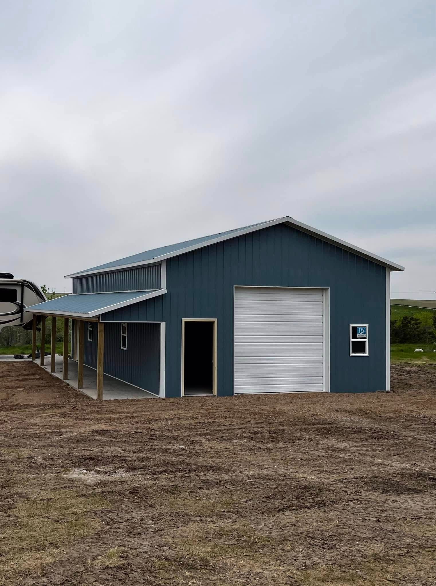 Blue metal building with a white garage door, open door, and covered porch.