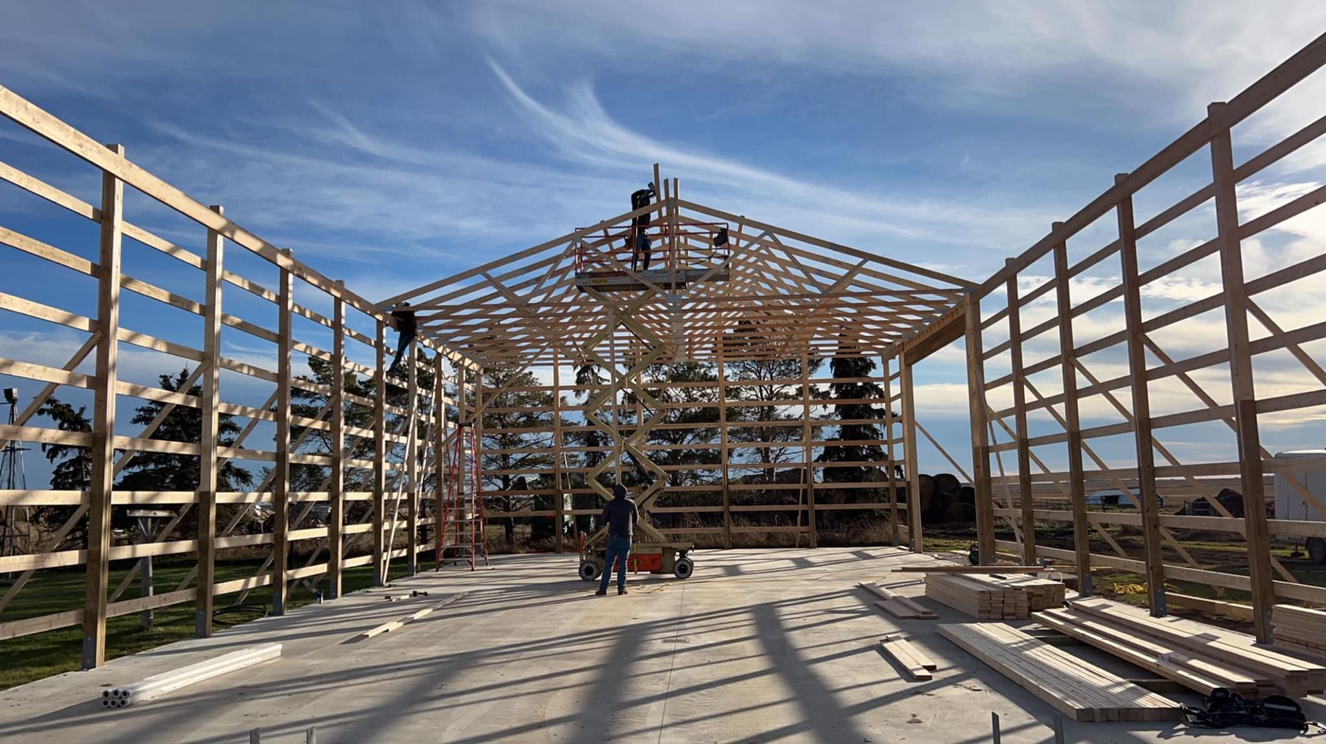 Construction of a wooden building frame; workers on the structure under a blue sky.