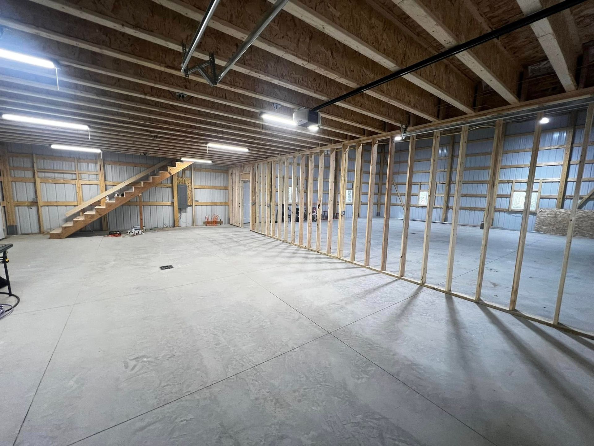 Interior view of a large unfinished garage with exposed wooden beams, concrete floor, and a framed wall.