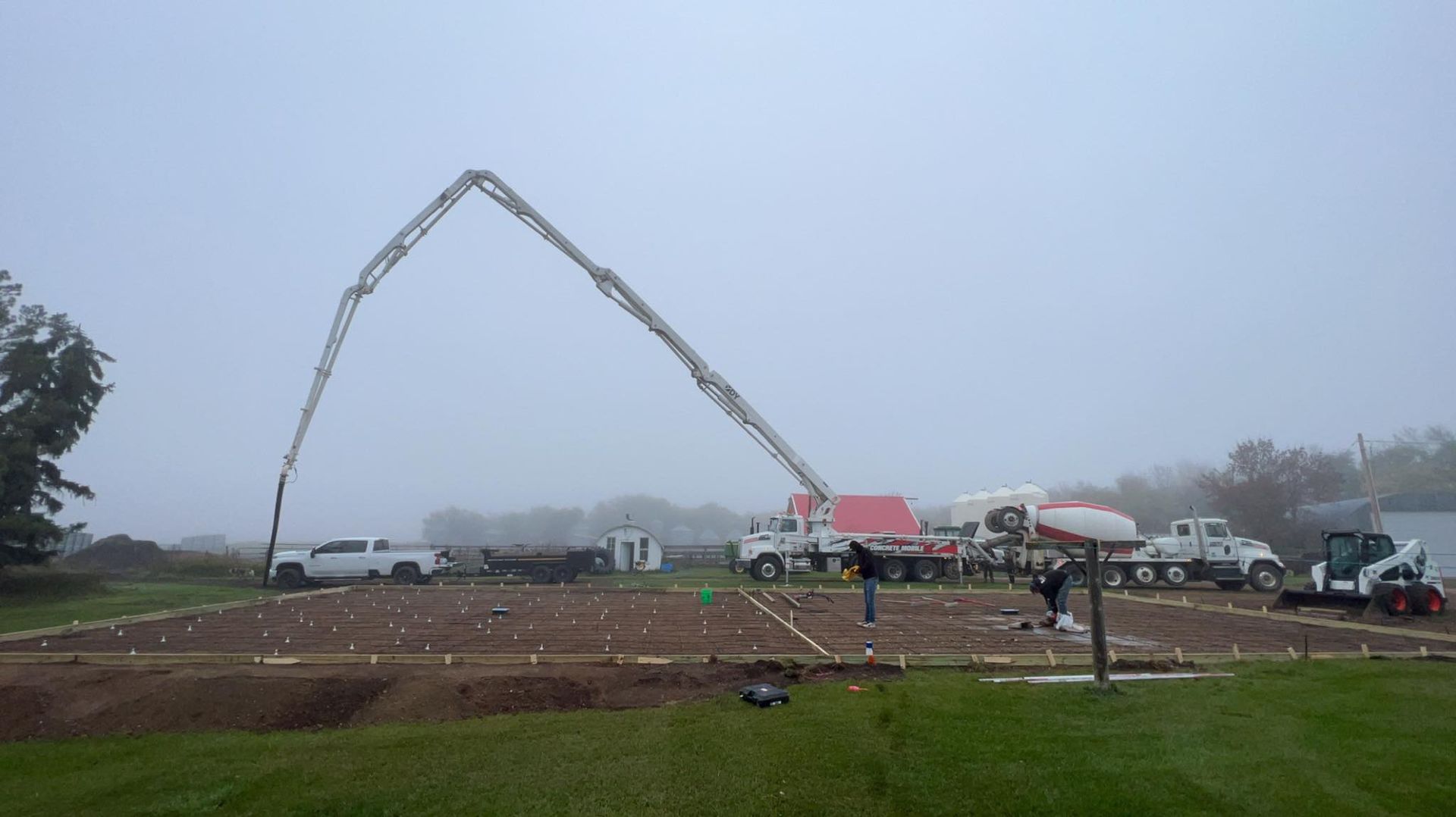Concrete pour at a construction site on a foggy day. A boom pump pours concrete into a prepared foundation.
