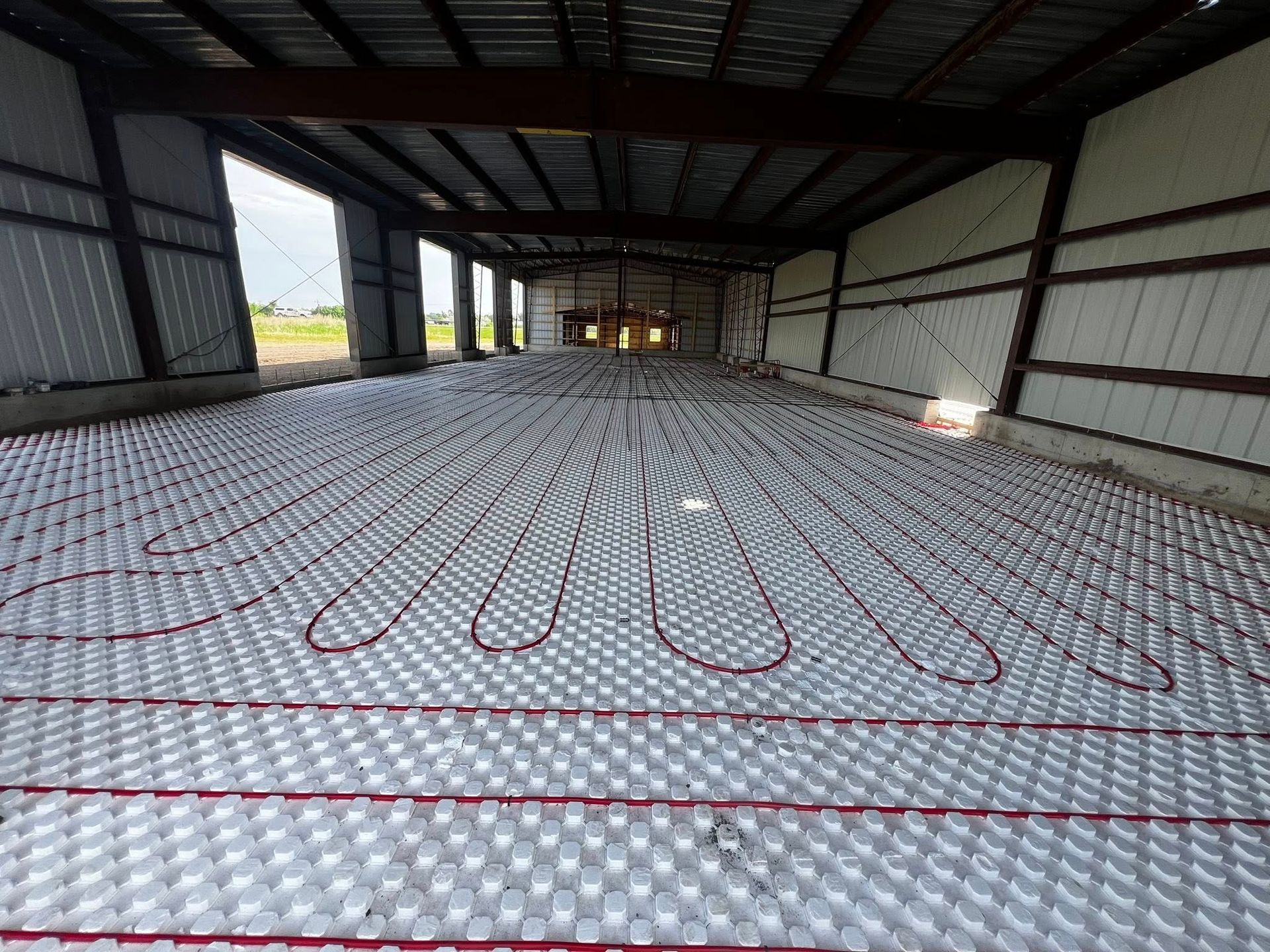 Red tubing laid in a pattern over white insulation on a concrete floor inside a large metal building.