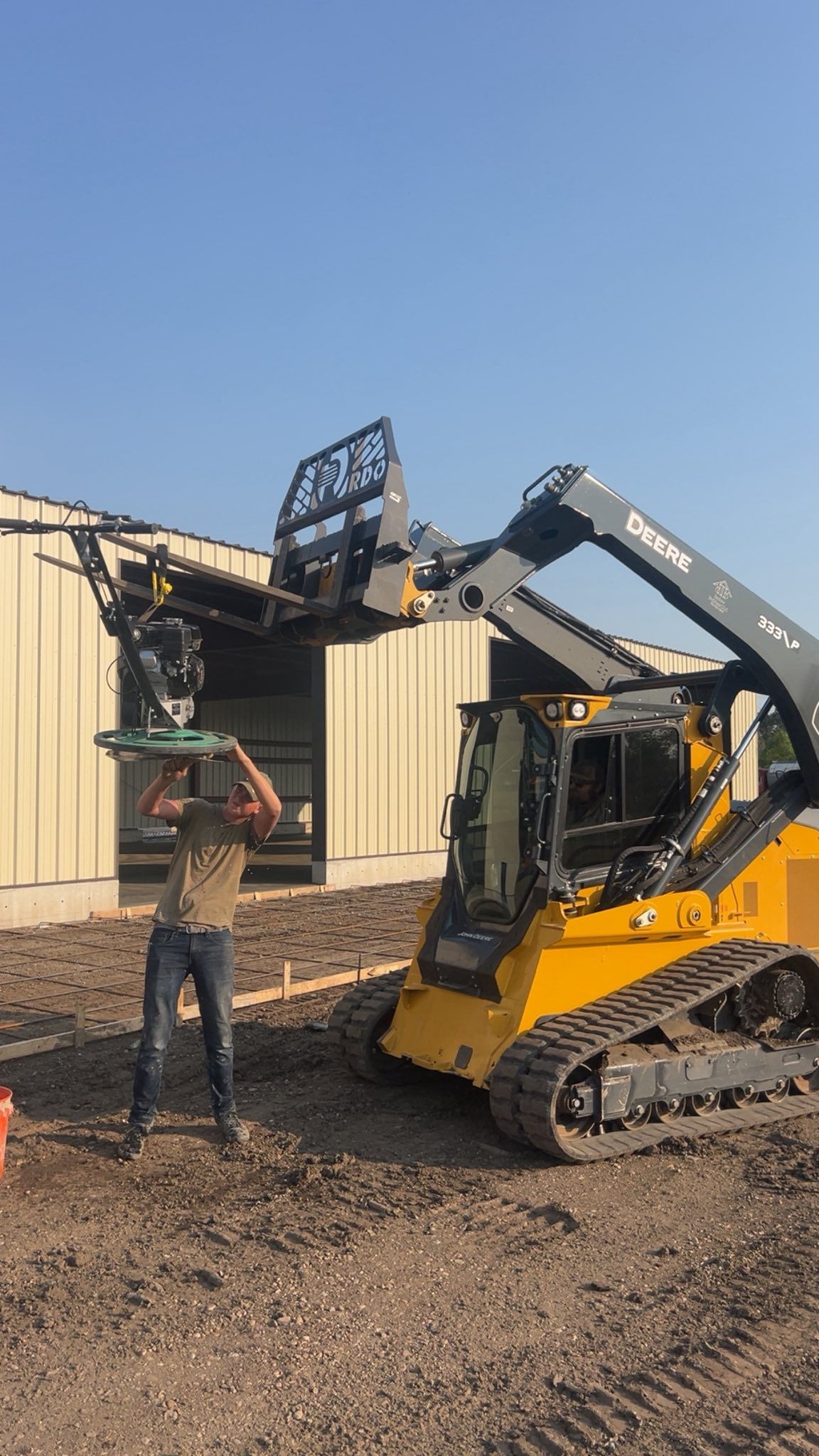 Man and yellow skid steer lift material at a construction site.