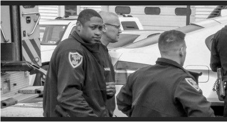 Police officers near a tow truck; one looks at the camera. Black and white.