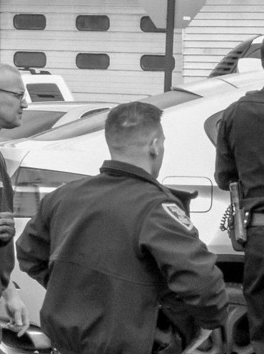 Three men near an airplane; one man is wearing a uniform and looking towards the plane.