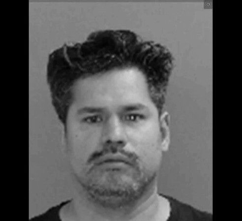 Mugshot of a middle-aged man with dark hair and a beard, in a black and white portrait.