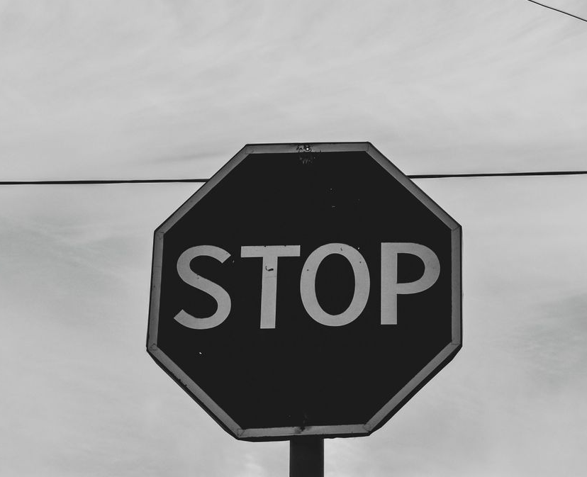 Black and white photo of a stop sign against a cloudy sky, featuring the word STOP in large white letters.
