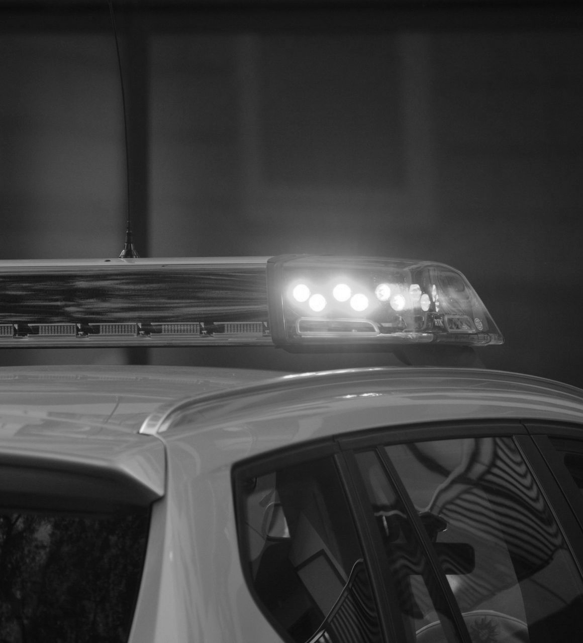 Black and white photo of a police car's roof with emergency lights illuminated.