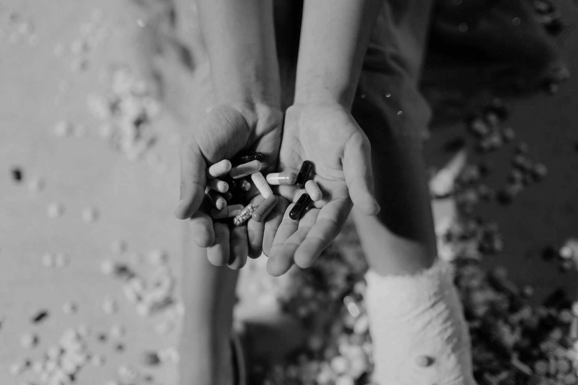 Hands holding pills, scattered pills around legs, leg in cast.