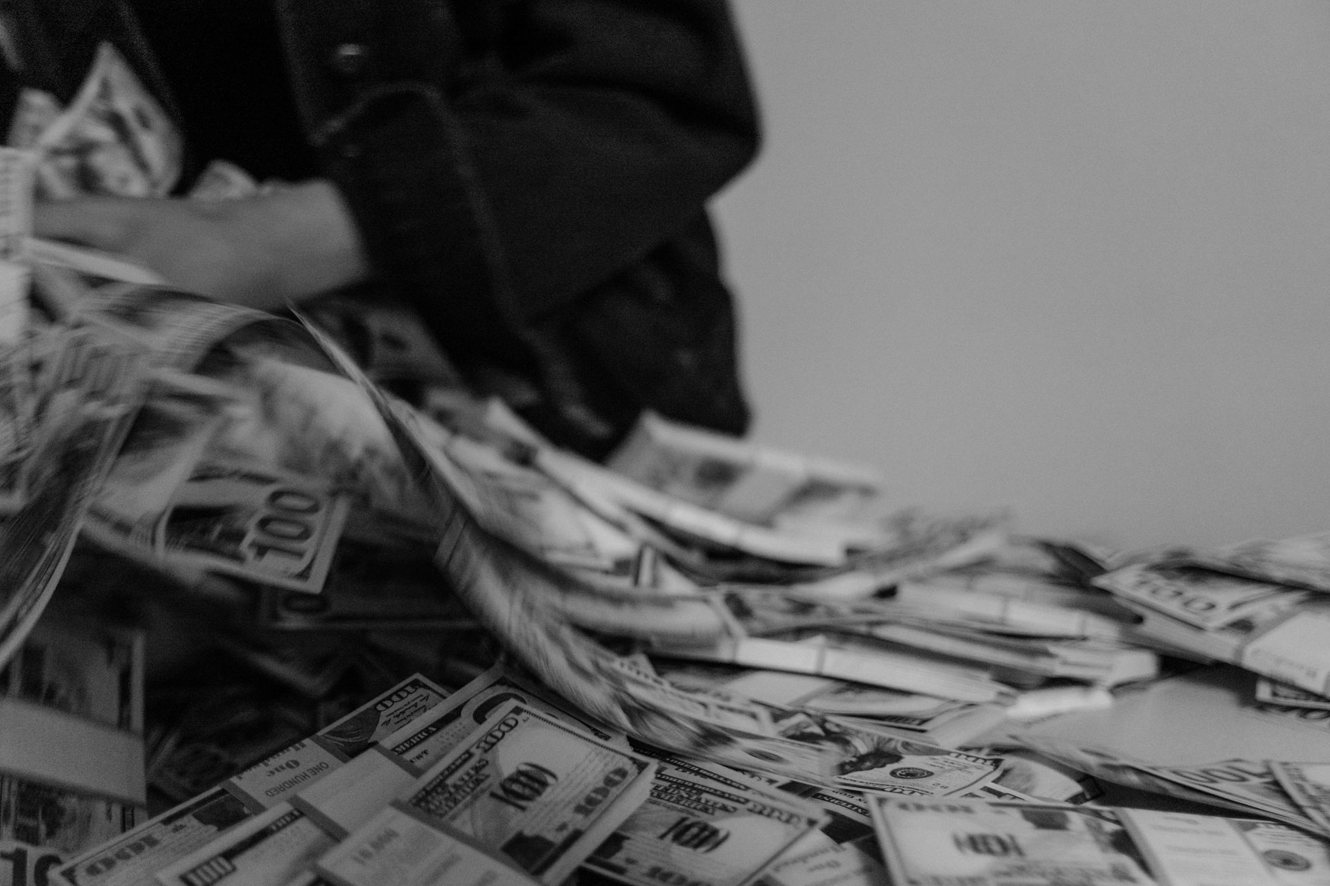 Person counting a large pile of hundred-dollar bills. Black and white photo.