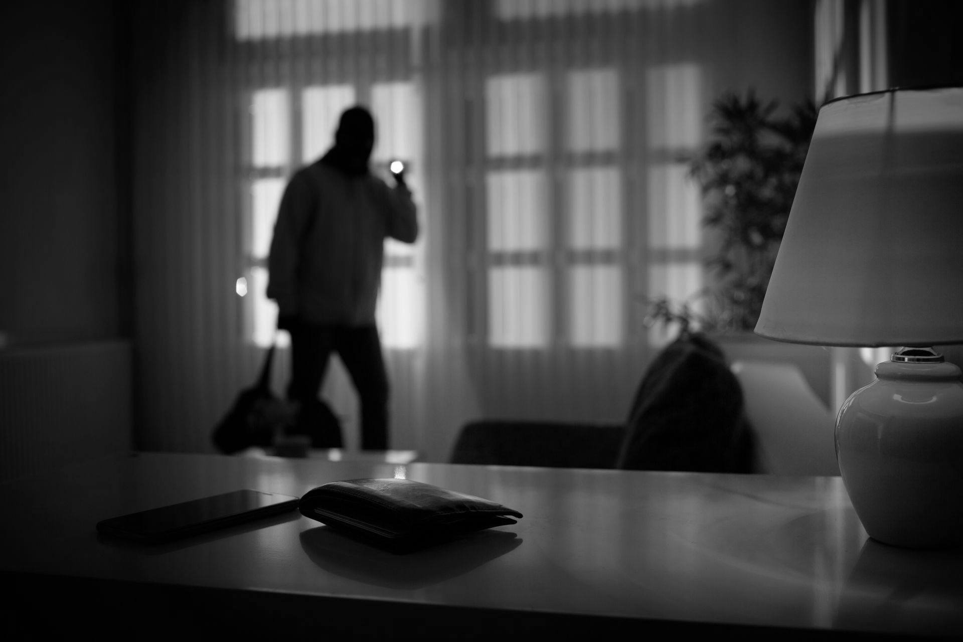 Burglar inside a house, holding a flashlight, wallet and phone in focus on table.