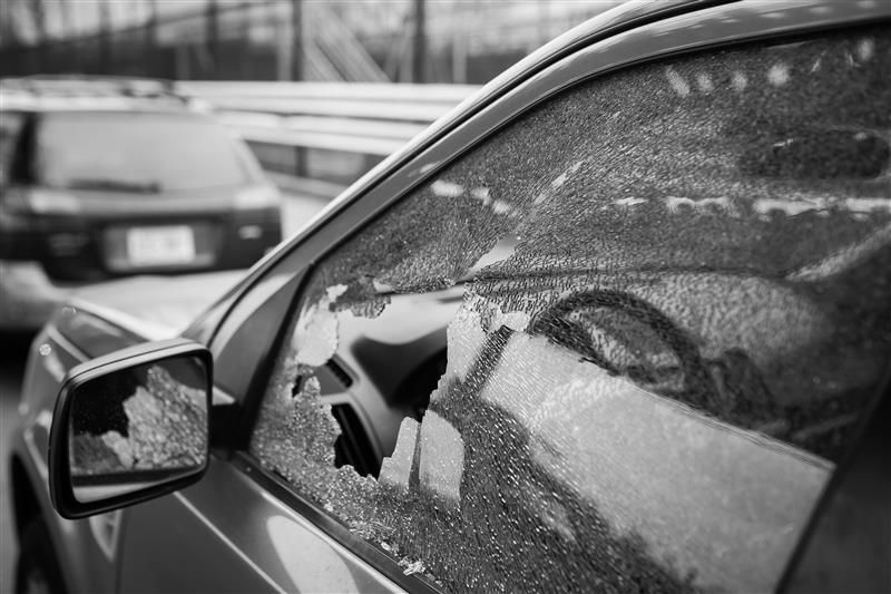 Black and white shot of a car with a shattered side window, suggesting a break-in.