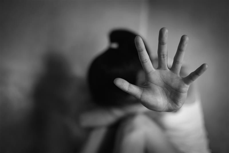 Woman with hand raised in a stop gesture, possibly in distress, in grayscale.
