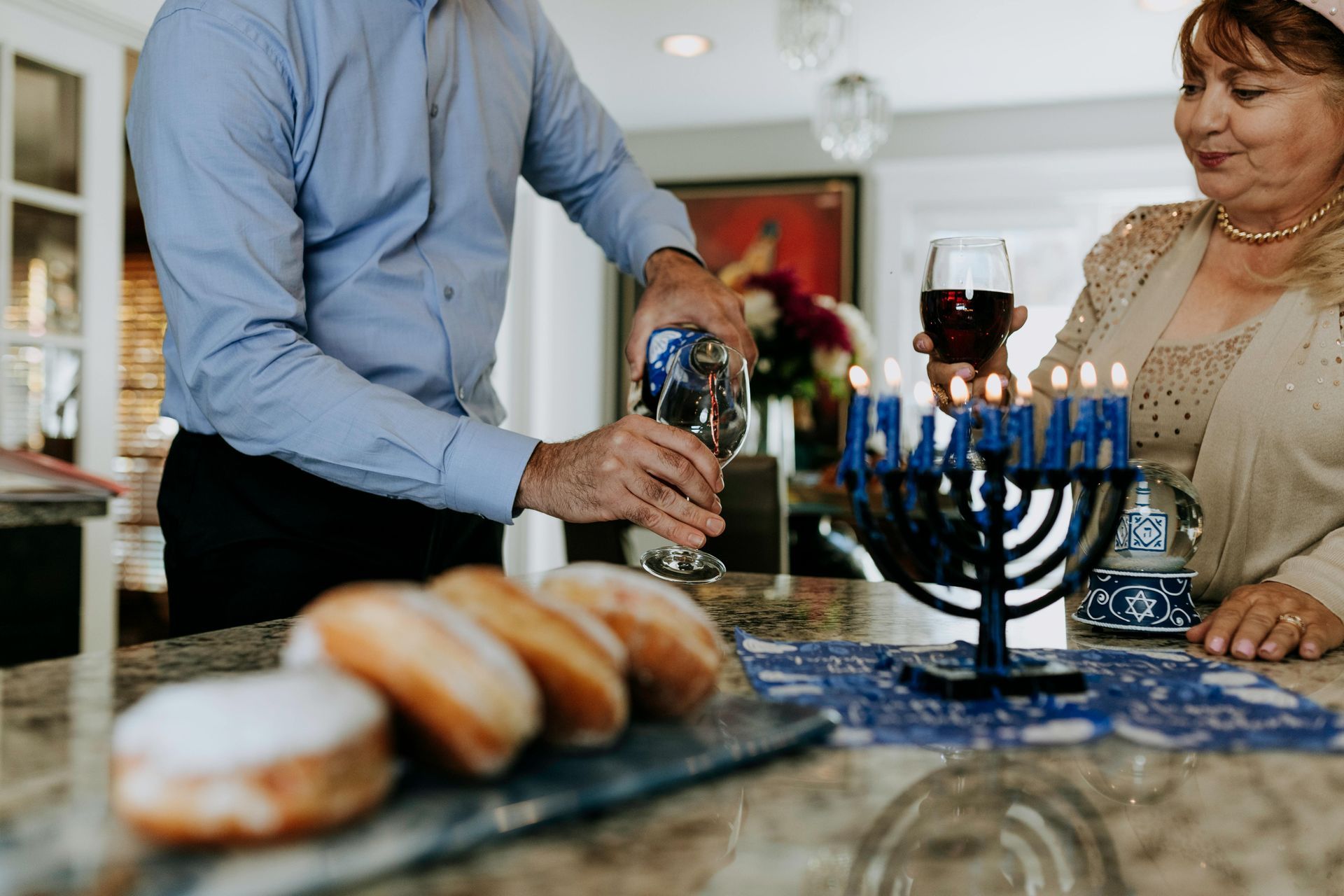 שני אנשים מדליקים חנוכייה עם סופגניות, יין ונרות על דלפק.