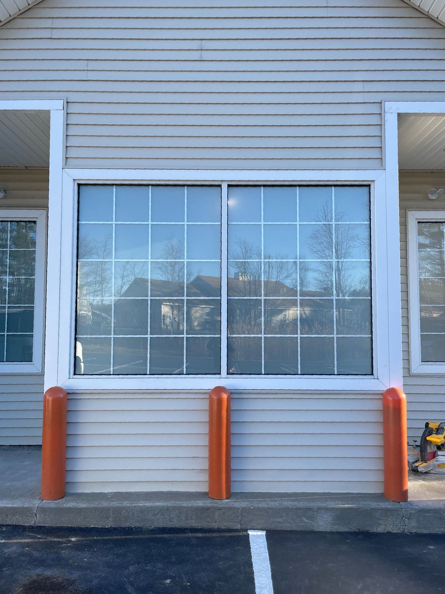 Exterior of building with large window, orange bollards, and horizontal siding. Reflection of trees and building in glass.