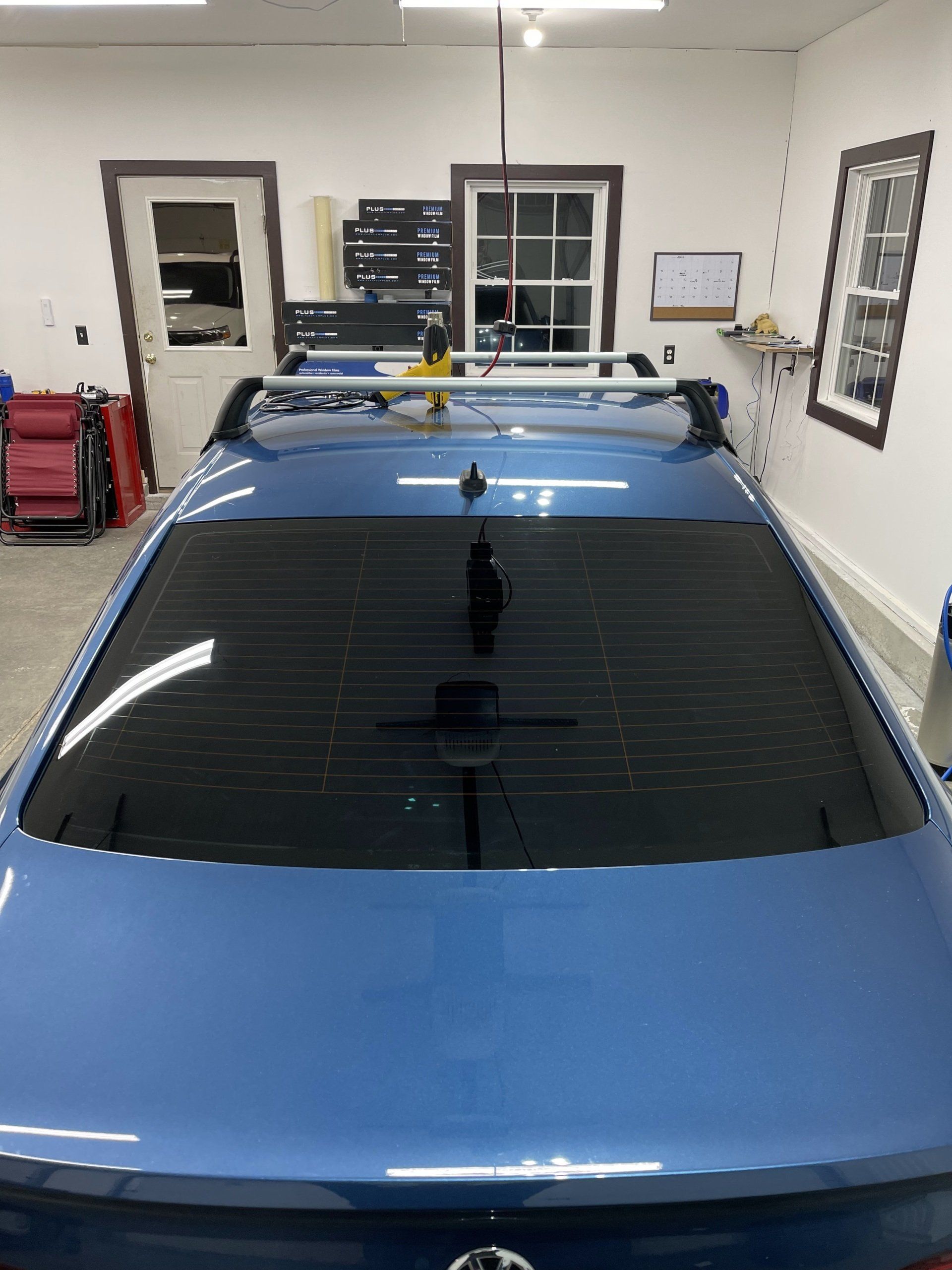 Two black-framed windows look out onto a wooden deck with a white chair and a green forest backdrop.