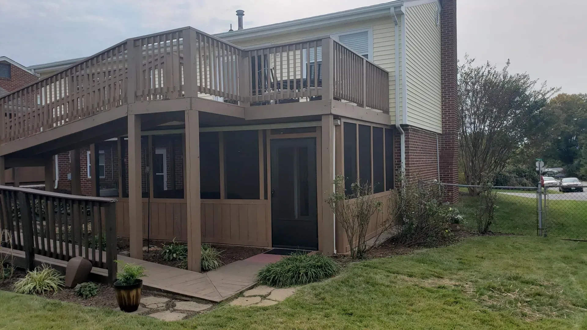 Two-story house with wooden deck, screened-in porch, and walkway on a grassy lawn.